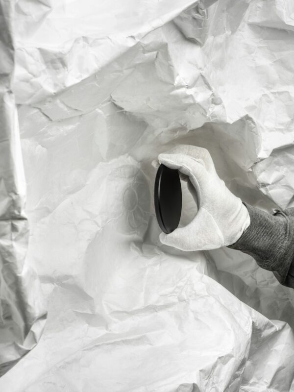 Mână cu mănușă ținând obiect negru rotund